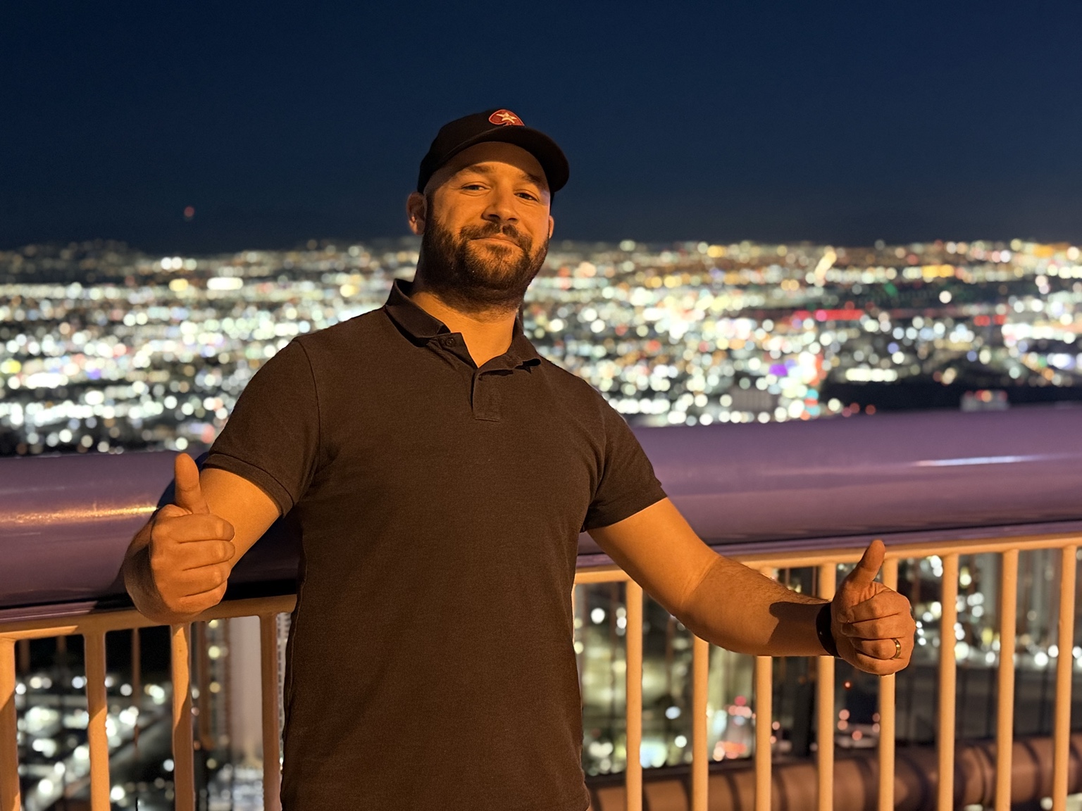 Chris giving two thumbs up with a nighttime city skyline behind him