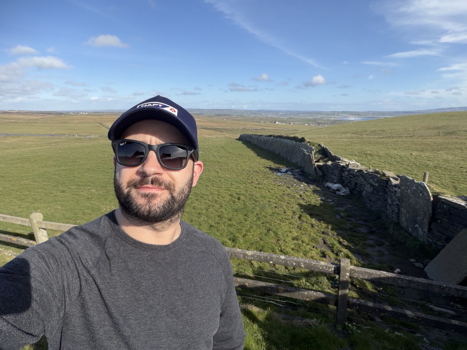 Chris outdoors with green fields and a stone wall