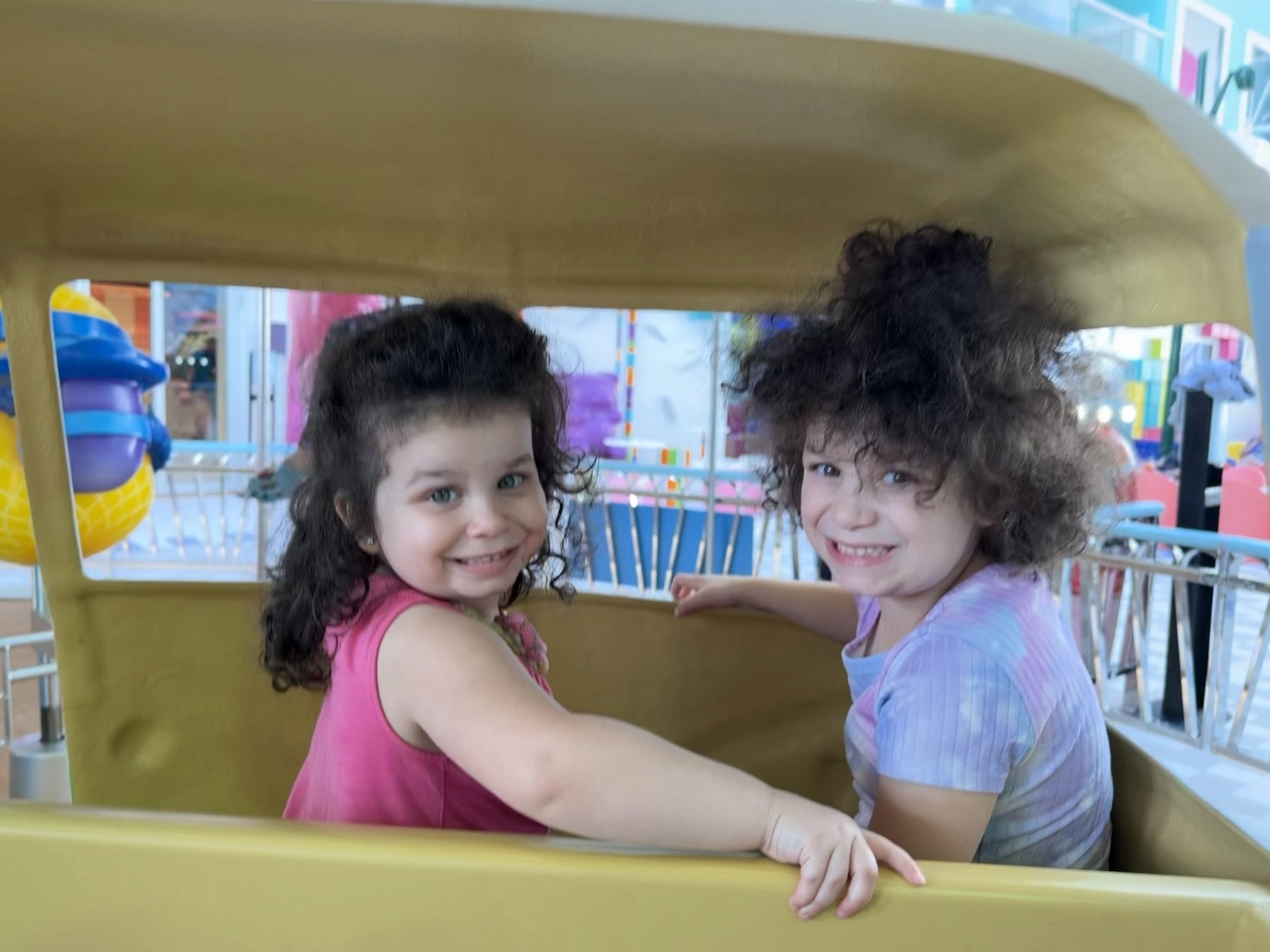 Two daughters smiling in a yellow amusement ride vehicle